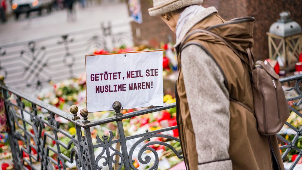 Eine Frau steht auf dem Marktplatz am Denkmal der Brüder Grimm, an dem die Bürger mit Blumen, Plakaten und Kerzen ihre Trauer zum Ausdruck bringen. An einem Plakat steht die Aufschrift "Getötet, weil sie Muslime waren"; © dpa/Frank Rumpenhorst