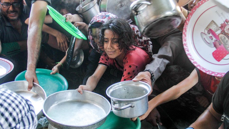 Kinder strecken ihre Gefäße aus, um in der Stadt Beit Lahia im nördlichen Gazastreifen Nahrung zu bekommen, Juli 2024; © picture alliance/dpa/XinHua/Mahmoud Zaki