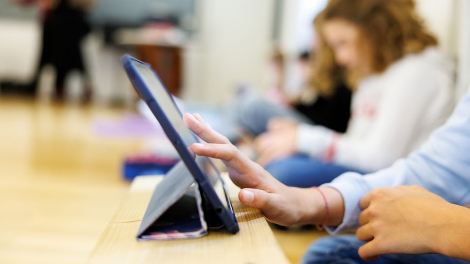 Eine Schülerin einer sechsten Klasse sitzt mit anderen Schülerinnen in einem Schulraum und arbeitet an ihrem Tablet. © picture alliance/dpa/Matthias Balk