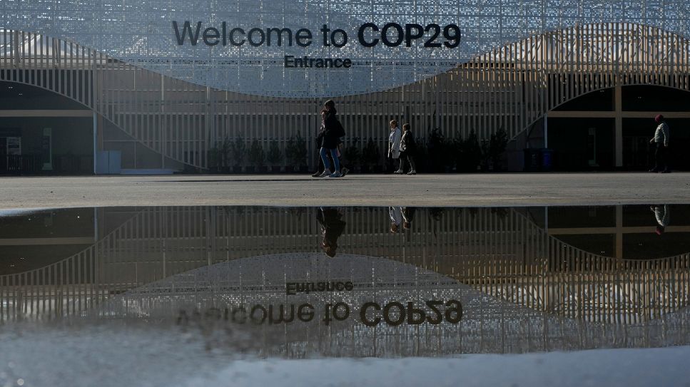 Menschen gehen in der Nähe des Eingangs zum UN-Klimagipfel COP29 spazieren. © picture alliance/dpa/AP | Rafiq Maqbool