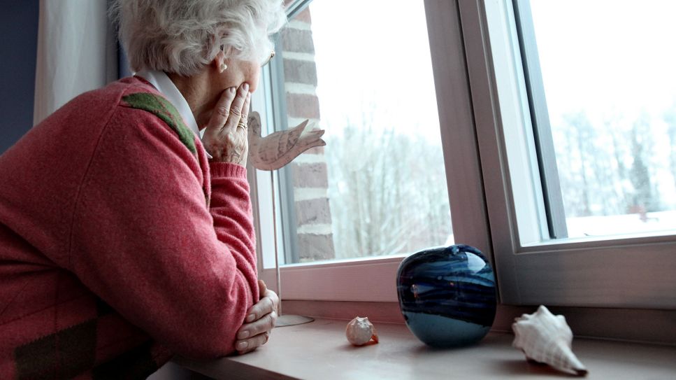 Eine ältere Frau schaut aus dem Fenster eines Hauses; © picture alliance/dpa/Bodo Marks