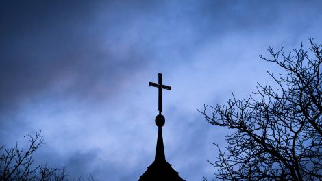 Dunkle Wolken ziehen über das Kreuz auf einer evangelischen Kirche hinweg; © picture alliance/dpa/Julian Stratenschulte