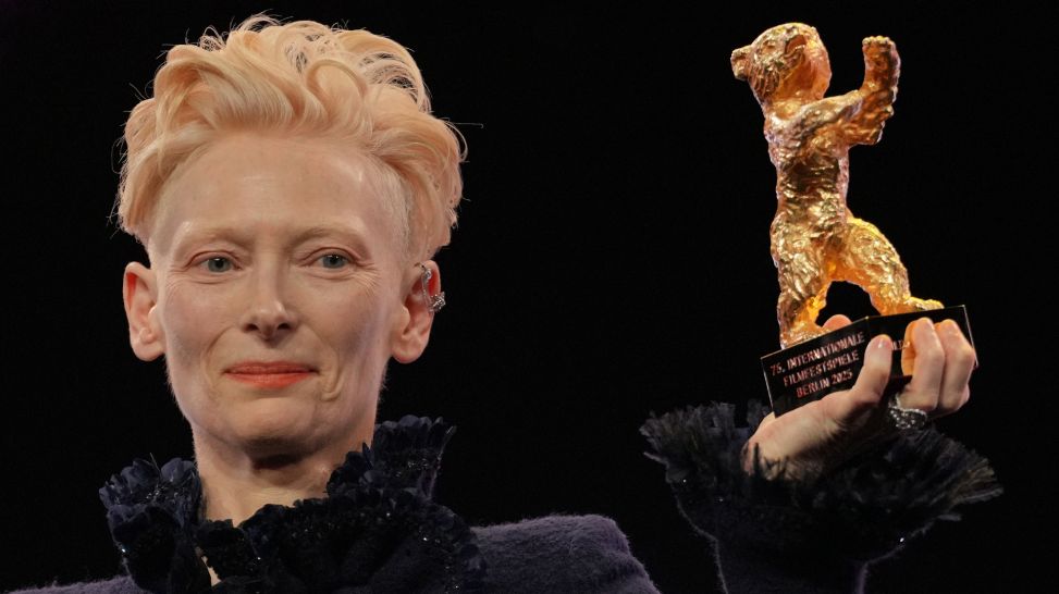 Tilda Swinton steht während der Eröffnung der Berlinale auf der Bühne und hält ihren Goldenen Ehrenbär, 13.02.2025; © picture alliance/dpa/Soeren Stache