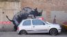 Banksy – Nashorn an einer Hauswand, davor ein defekter Kleinwagen, Westmoor Street in Charlton, South East London; © picture alliance/dpa/Lucy North/PA