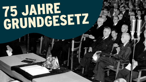 Unter einer schwarz-rot-goldenen Standarte liegt am 23.5.1949 das Grundgesetz der Bundesrepublik Deutschland auf einem Tisch im Sitzungssaal des Parlamentarischen Rates in Bonn; © picture-alliance / dpa